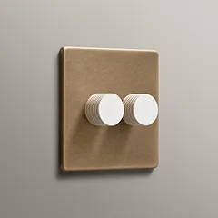 Antique Brass double dimmer with white knurled knobs on a neutral painted wall