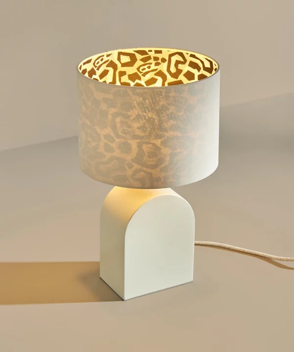 modern bedside table lamp with cream metal arch-shaped base and matching cream shade lined with animal print