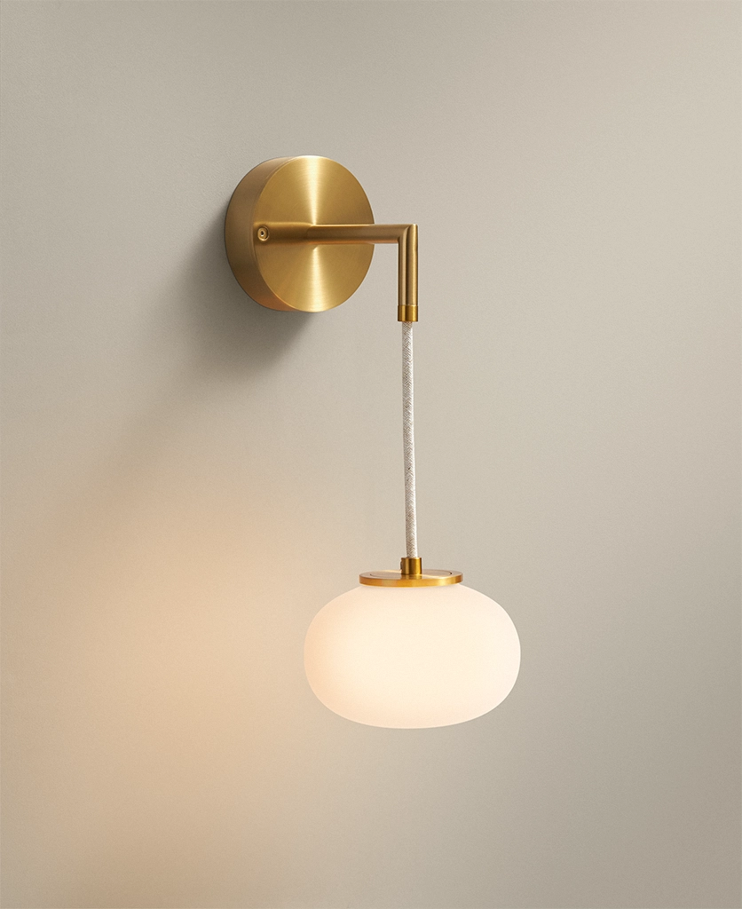brass wall light with opal glass shade hanging from linen cable