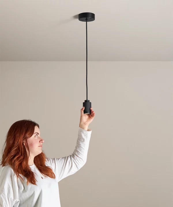 single black spotlight pendant with a woman reaching up to adjust it in a neutral painted room